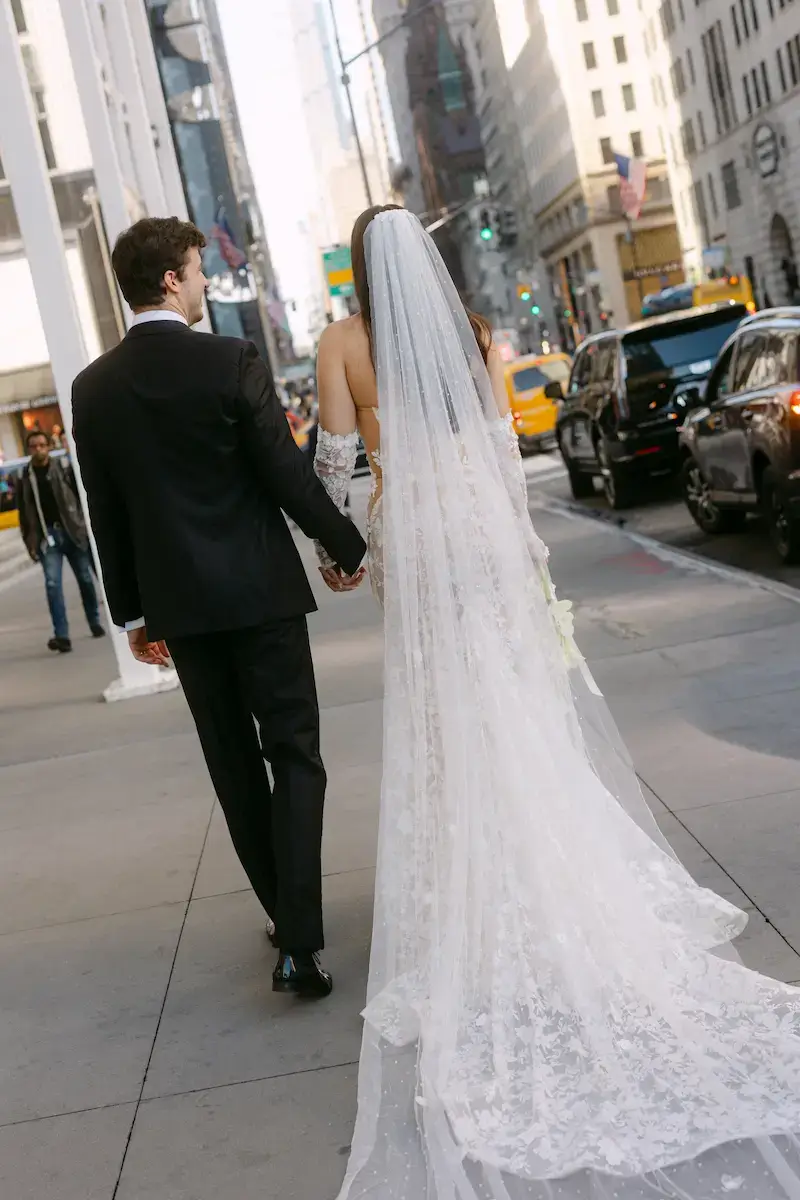 Walk into Forever – Branding-Motiv für Hochzeitsplaner:innen & Destination Weddings Braut mit langem Schleier und Bräutigam gehen Hand in Hand durch die Stadt – modernes Hochzeitsfoto mit Großstadtflair