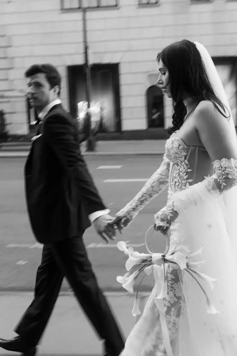 City Chic Wedding – perfekte Aufnahme für Editorial-Reels & Portfolioseiten Braut mit Statement-Kleid und Schleier, Paar läuft Hand in Hand – urbanes Hochzeitsfoto mit Dynamik
