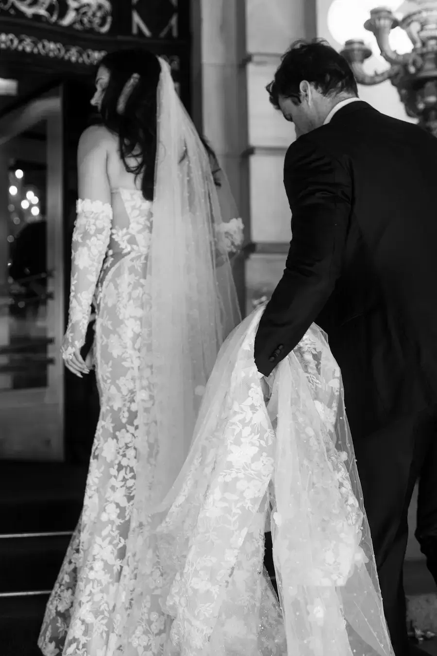 Authentisches Hochzeitsbranding: Schwarz-Weiß-Moment für stilvollen Contentaufbau Der Bräutigam hebt die Schleppe der Braut – eine klassische Szene, die für stilvolles Social Media Branding genutzt werden kann. Ideal für Wedding Planner:innen, Content Creators und Fotograf:innen, die emotionale Details sichtbar machen wollen.